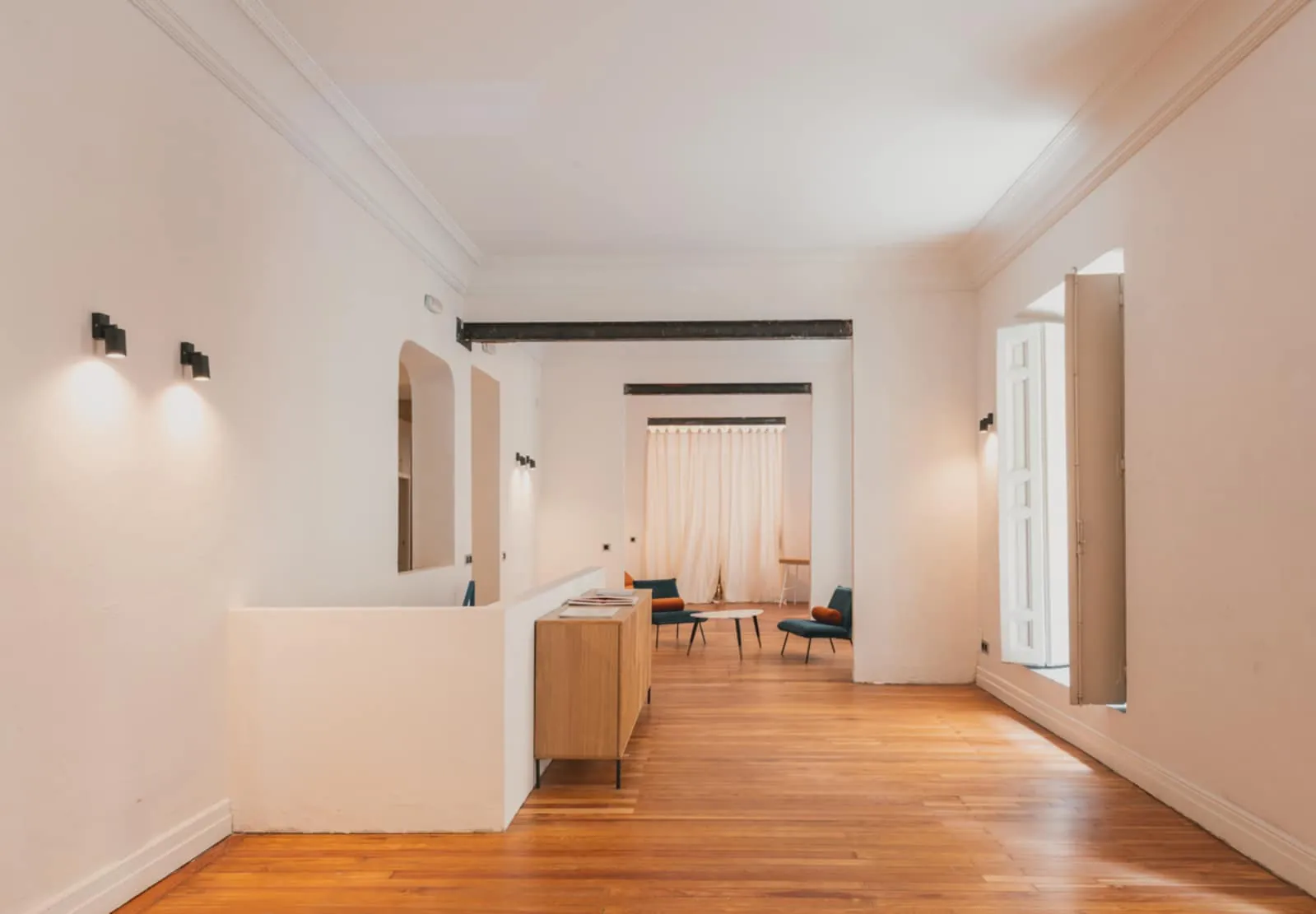 Galería blanca con suelo de madera y una enfilada de estancias hacia la luz