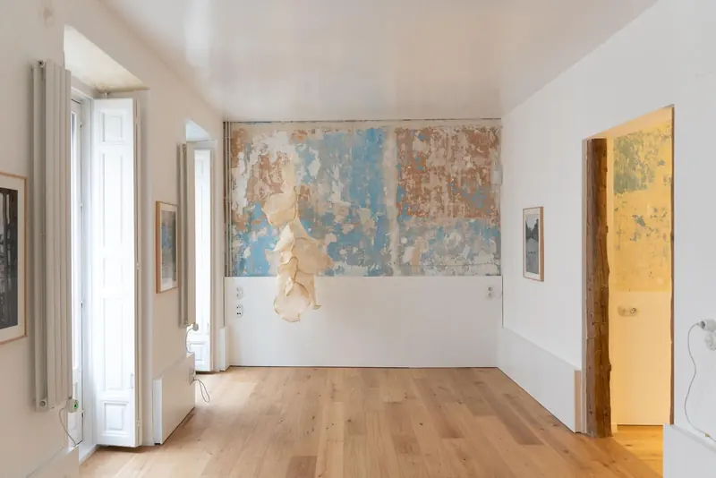 Estancia con muro de pintura antigua desconchada, obra textil y suelo de madera