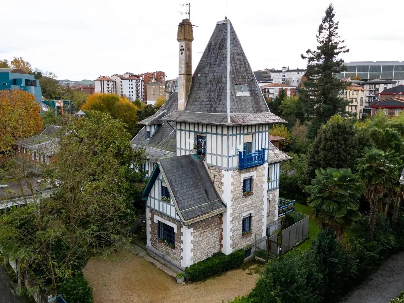 Villa de influencia normanda con torre de pizarra y entramado de madera entre árboles
